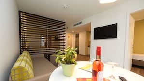 A modern living room with a sofa, a round table with a bottle, a remote control, and a potted plant.