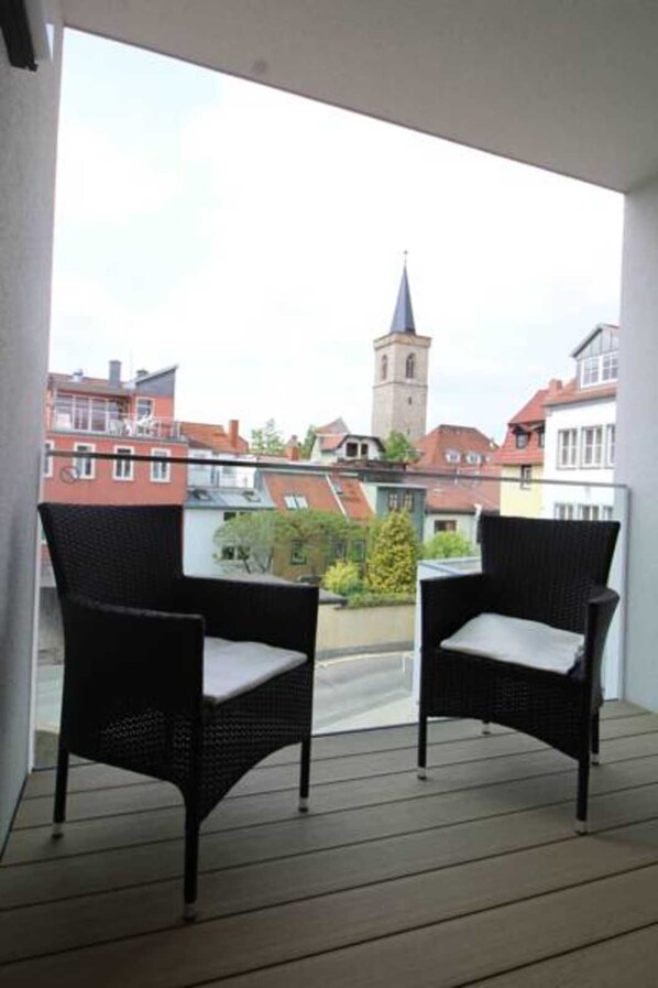 A balcony with two wicker chairs and a view of a town with a church tower.