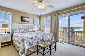 Een slaapkamer met een groot bed, een plafondventilator en uitzicht op het strand door de schuifdeur.
