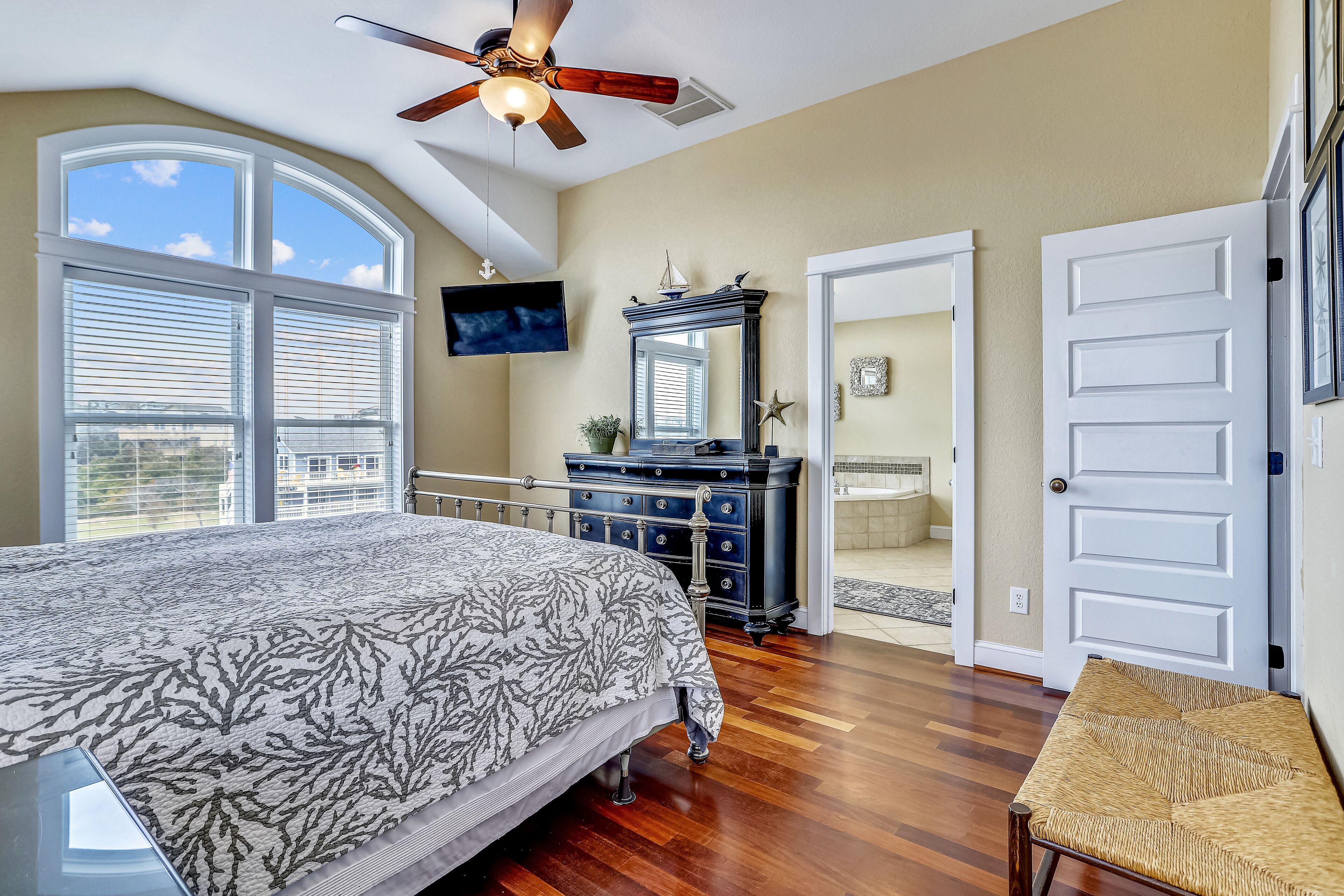 A bedroom with a large bed, a ceiling fan, a dresser, and a TV.