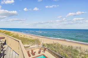 A beach view from a balcony with a pool and lounge chairs.