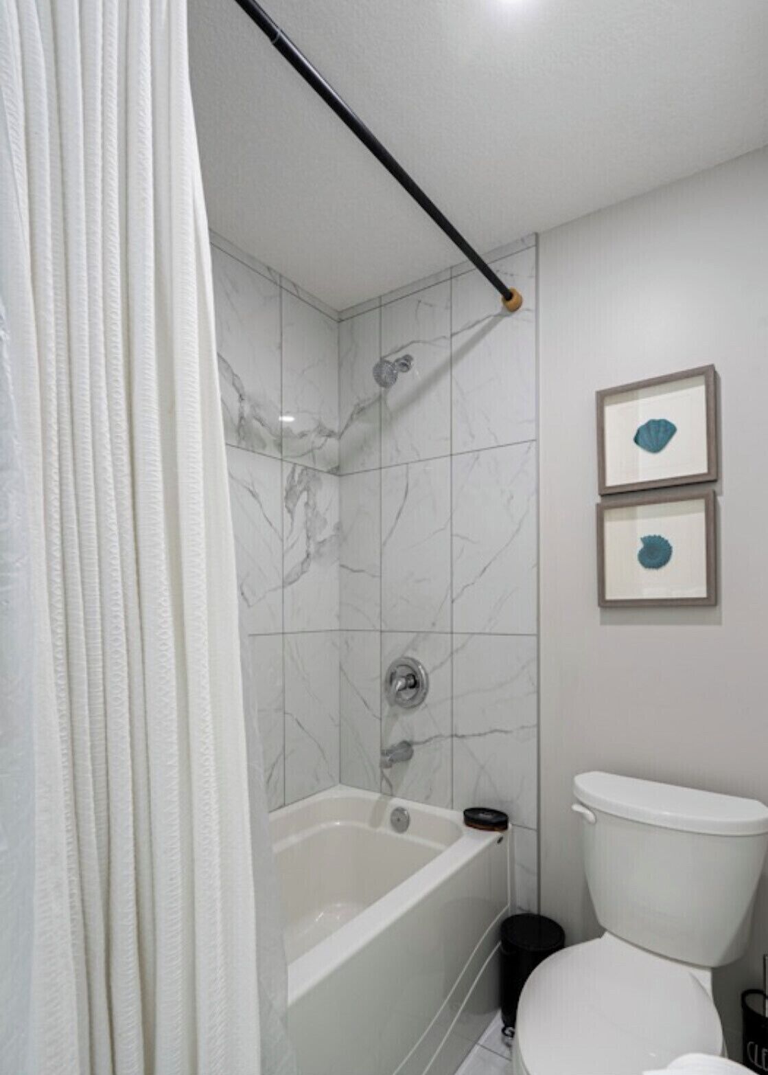 A bathroom with a bathtub, toilet, and two framed pictures on the wall.