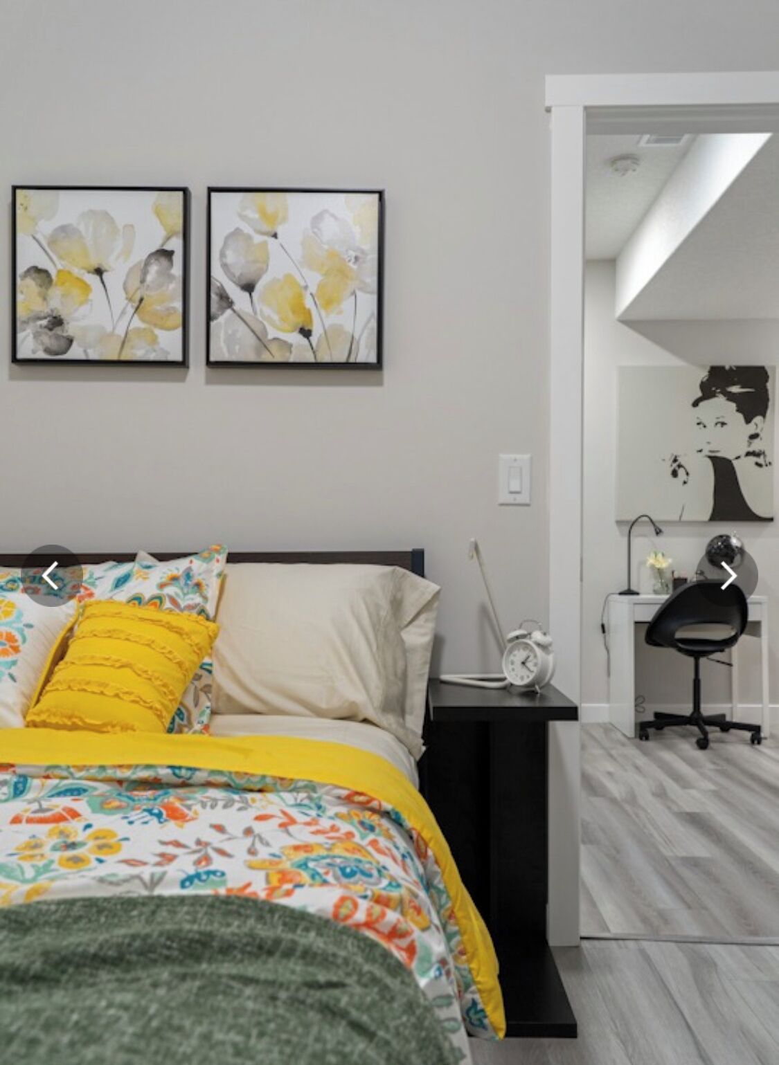 Une chambre à coucher comprenant un lit, une table de chevet, un bureau et une chaise. Deux œuvres d’art sont accrochées au mur au-dessus du lit.