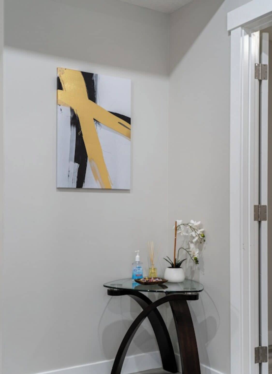A room with a modern abstract painting, a small round table with a potted plant and a bottle of hand sanitizer.
