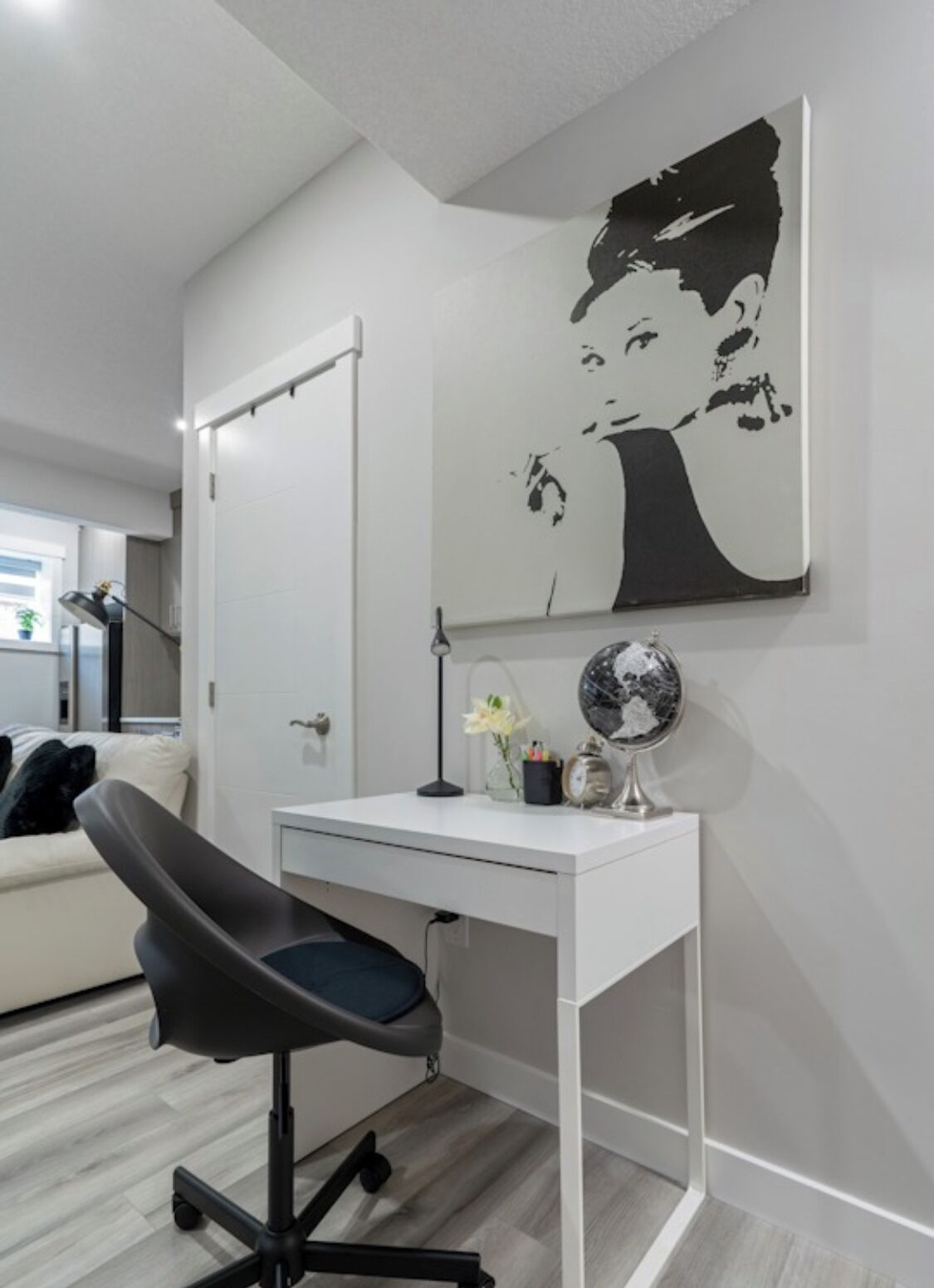 Une chambre moderne avec un bureau blanc, un fauteuil de bureau noir, un grand miroir et une œuvre d’art en noir et blanc accrochée au mur.