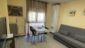 A living room with a grey sofa, a dining table with chairs, a radiator, and a television.