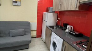 A compact kitchenette with a washing machine, a small refrigerator, a microwave, and a coffee maker.