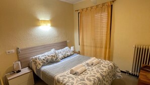 A neatly made bed with patterned bedding, a bedside table with a lamp, and a window with curtains.