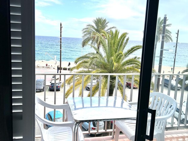A balcony with a table and chairs, overlooking a beach with palm trees and the ocean.