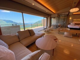 A modern interior with a large sofa, round tables, wicker chairs, and a view of mountains through large windows.