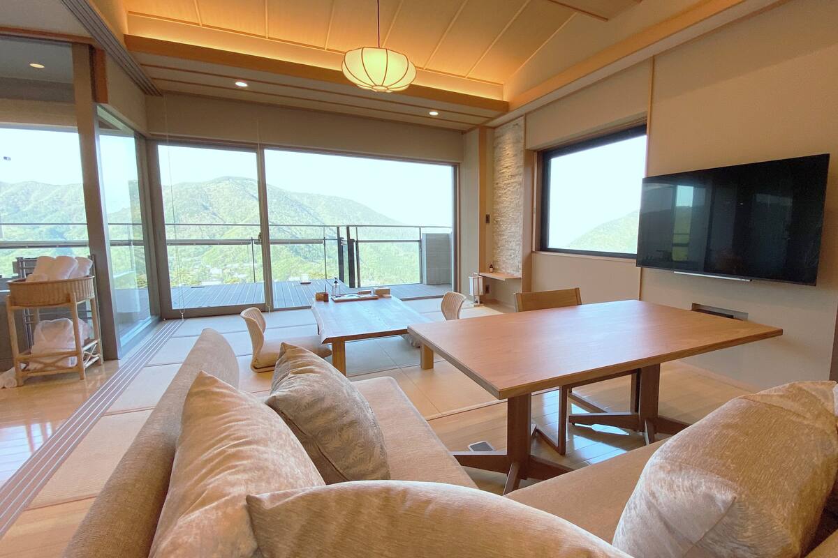 A modern living room with a large TV, comfortable seating, and a view of the mountains.