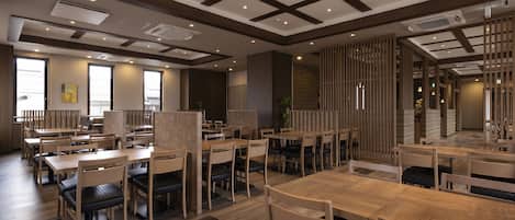 A spacious restaurant with wooden tables and chairs, large windows, and a modern ceiling design.