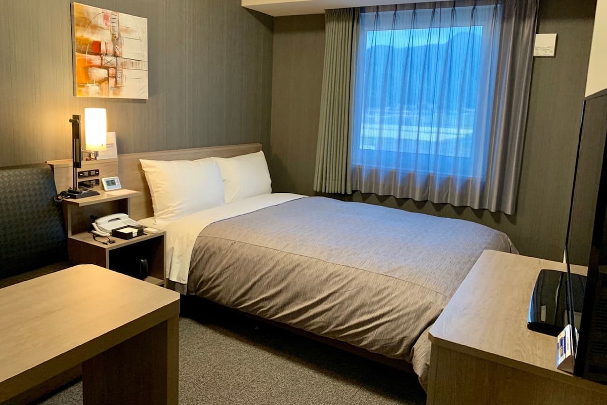 A hotel room with a bed, bedside table, lamp, and a painting on the wall.