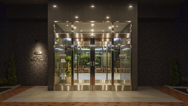 A hotel entrance with a modern design, featuring a glass door and a sign indicating amenities like a cool and warm business center. - Hotel Route-Inn Yonago (Yonago)