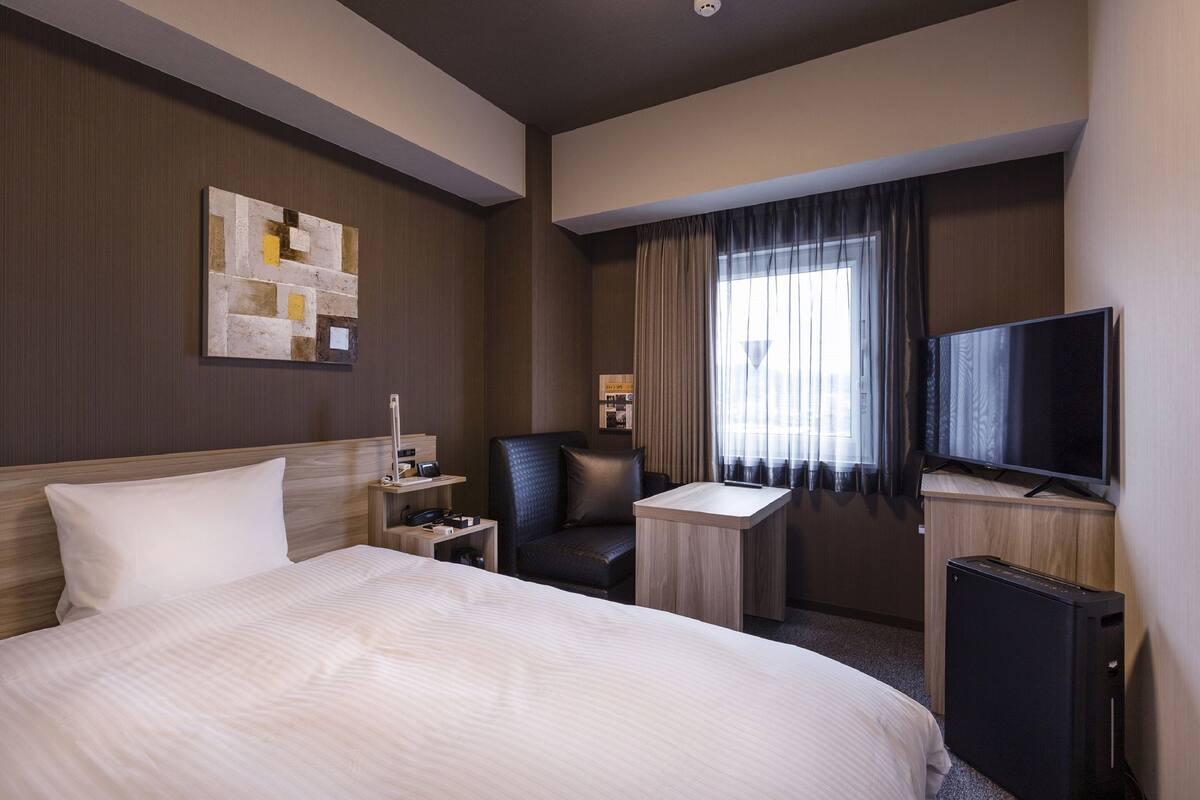 A hotel room with a large bed, a desk, a chair, a television, and a wall-mounted artwork.
