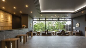A modern hotel lobby with a reception desk, seating area, and large windows offering a view of greenery. - Hotel Route-Inn Yonago (Yonago)