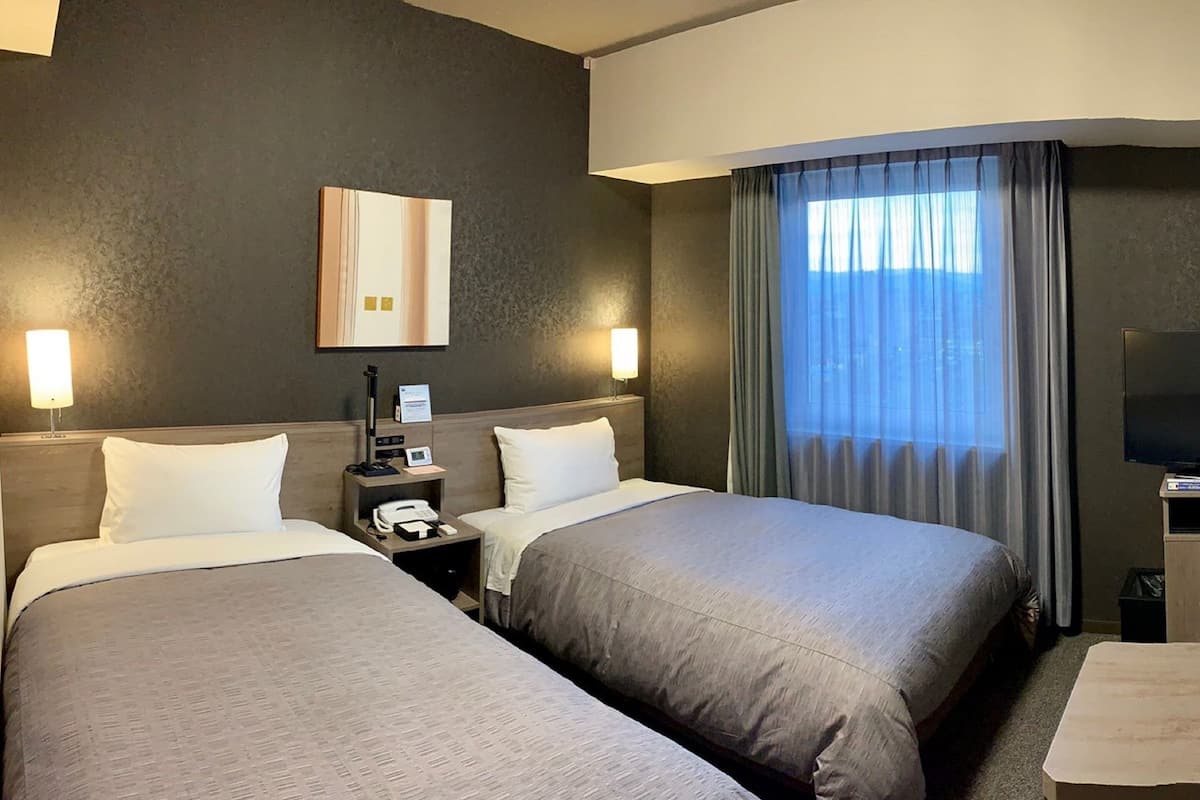 A hotel room with two beds, a nightstand with a phone, a lamp, and a TV.