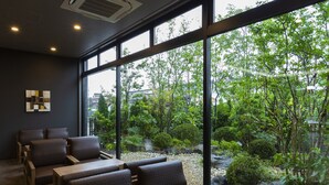 A modern interior with large windows, seating area, and a view of a landscaped garden. - Hotel Route-Inn Yonago (Yonago)