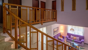 Ein mehrgeschossiges Interieur mit einer Holztreppe, einer violetten Sofagarnitur und einer hängenden Leuchte.
