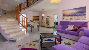 Ein geräumiger Wohnbereich mit Treppe, einem violetten Sofa, einem Strandbild und einem Essbereich.