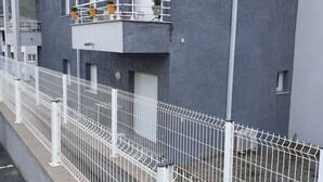 A multi-story residential building with balconies, a white metal fence, and a grey exterior.