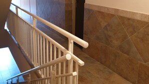 A staircase with a white handrail, beige walls, and a tiled floor.
