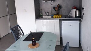 A compact kitchen with a microwave, sink, and a small refrigerator. There is a dining table with chairs and a bottle of water on the table.