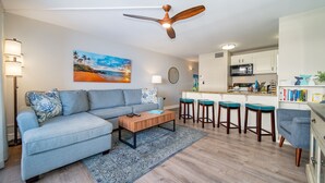A modern living room with a sofa, coffee table, and a painting of a beach. - Big Ocean View from your Sugar Beach Retreat -King Bed, Central AC, WiFi  #208 (Kihei)