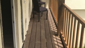 Una terraza de madera con una silla y una mesa, baranda de madera y pared blanca.
