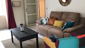 Una sala de estar con un sofá marrón, almohadones coloridos, una mesa de centro negra y una cortina roja.