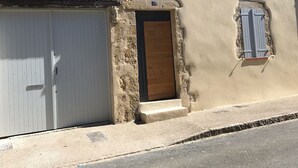 Un edificio con fachada color beige, una gran puerta de garaje blanca y tres ventanas con contraventanas.