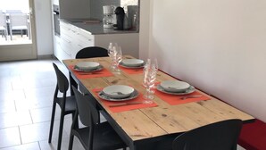 Un comedor con una mesa de madera larga preparada para cuatro personas, sillas negras y una cocina al fondo.