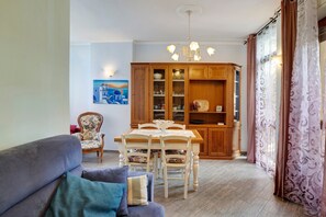 Un comedor con mesa y sillas de madera, un sillón estampado y un aparador con puertas de cristal.