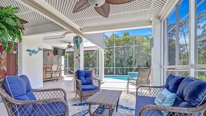 A covered outdoor area with wicker furniture, a pool, and a view of palm trees. - TWO-LEVEL SCREENED LANAI & HEATED POOL | SEPARATE LOWER SUITE | BONITA SPRINGS CANAL HOME (Bonita Springs)