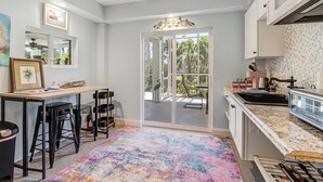 A modern kitchen with a large window, a colorful rug, and a dining area with chairs. - TWO-LEVEL SCREENED LANAI & HEATED POOL | SEPARATE LOWER SUITE | BONITA SPRINGS CANAL HOME (Bonita Springs)