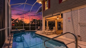 A swimming pool with a view of a sunset, outdoor seating, and a covered patio area. - TWO-LEVEL SCREENED LANAI & HEATED POOL | SEPARATE LOWER SUITE | BONITA SPRINGS CANAL HOME (Bonita Springs)