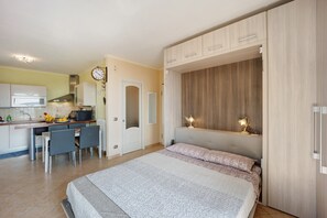 A bedroom with a bed, a desk with chairs, a kitchenette, and a clock on the wall. - Pet-Friendly Apartment Maison Laura with Sea View, Wi-Fi, Terrace & Garden (Diano Arentino)