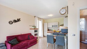 Ein Wohnzimmer mit rotem Sofa, einem Essbereich mit Stühlen, einer Küche mit Schränken und einer Wanduhr.