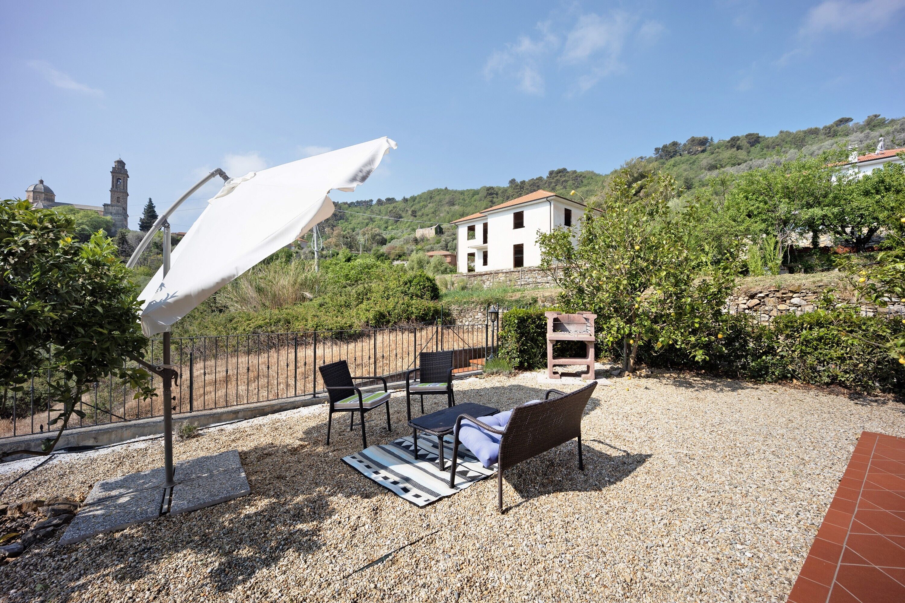 A patio with outdoor furniture, a white umbrella, and a view of a hill with a building.
