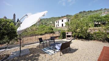A patio with outdoor furniture, a white umbrella, and a view of a hill with a building.