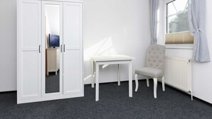 Een kamer met een witte kledingkast, een tafeltje, een stoel en een raam met gordijnen.
