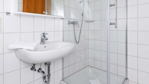 Een moderne badkamer met een douchecabine van glas, een witte wastafel en een spiegel boven de wastafel.