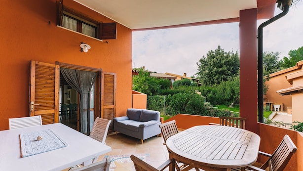 Een balkon met een tafel, stoelen, een bank en uitzicht op groen en gebouwen.