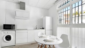 A modern kitchen with a built-in washer, a dining table with chairs, and large windows.