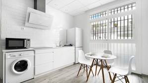 A modern kitchen with a washing machine, microwave, and dining area with white chairs.