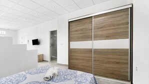 A bedroom with a bed, a wooden wardrobe, a television, and a bathroom visible in the background.