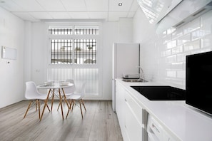 Une cuisine moderne avec des meubles blancs, une cuisinière noire et un coin repas avec des chaises blanches.