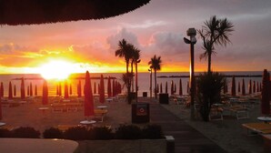 A beach with rows of sun loungers and umbrellas, palm trees, and a sunset in the background. - Luisa 5B - Cozy three rooms apartment (Lido di Pomposa)