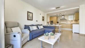 A modern living room with a sofa, armchair, and coffee table. There is a kitchen area with a dining table and cabinets. - MARJALETA, Beautiful apartment in the centre of Moraira for 4 pax free wifi. (Moraira)