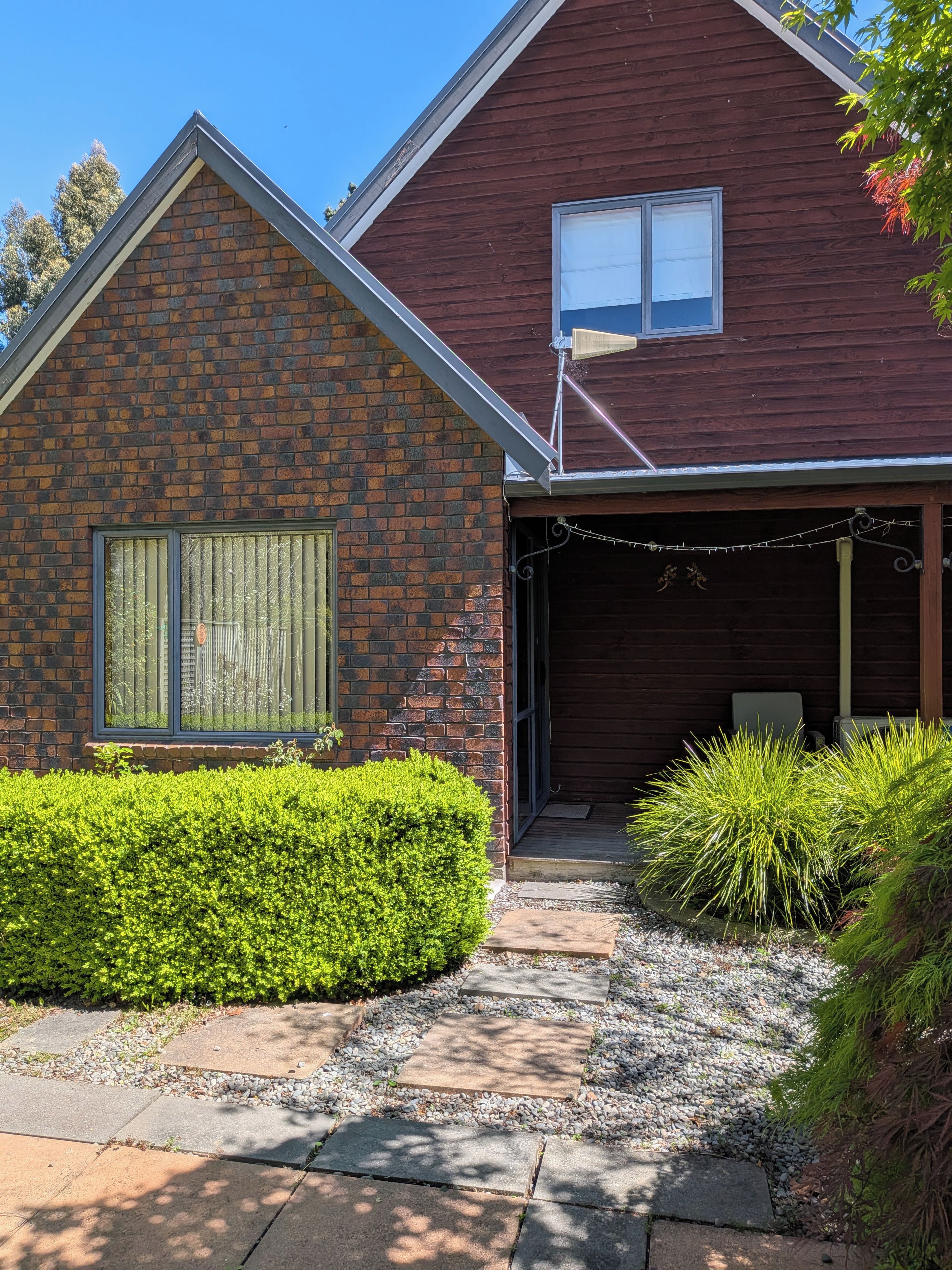 Une maison à deux étages avec une façade en briques, un garage fermé et un jardin bien entretenu, agrémenté de haies et de chemins de gravier.